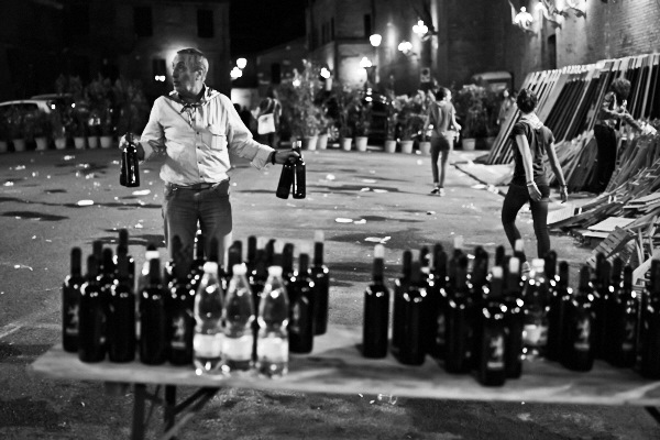 Fine art black and white photography of people in the street of Siena drinking wine after the Palio 2014