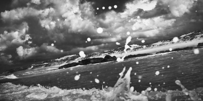 Fine art black and white photo of a seascape taken in Praia do Malhào in Portugal. The image is taken from inside the water of the ocean while a wave was breakin