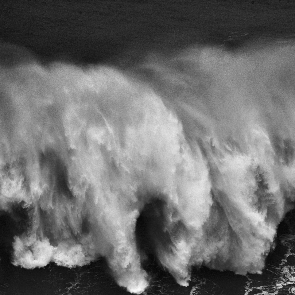 fine art black and white image of a big wave crashing in front of the lighthouse of Nazarè in Portugal 